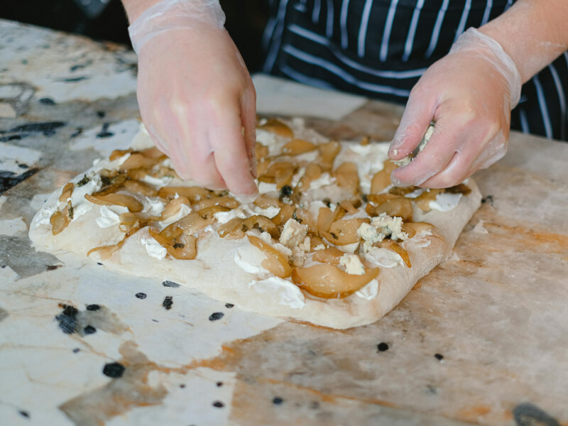 Gloved hands putting toppings on focaccia dough
